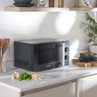 Dark grey microwave with silver handle on kitchen worktop, food and utensils beside