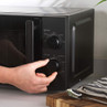Black microwave oven, close-up of hand turning timer dial on countertop