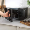 Black microwave on kitchen counter with door open, hand holding handle