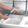 Flexible bottle brush cleaning a glass jar at sink under running water