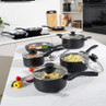 Black non-stick saucepan and frying pan set with glass lids shown in a modern kitchen