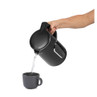 Hand pouring hot water from a black electric kettle into a matching mug