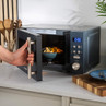 Grey microwave on countertop with door open, bowl of food inside, hand holding handle