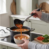 Black and silver ladle serving vegetable soup from pot to bowl in kitchen