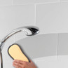 Yellow cleaning pad in use on bathroom tiles under shower head