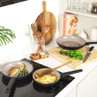 Set of cream non-stick frying pans on a hob with cooked food, bowl and board with broccoli