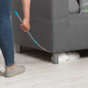 Dusting tool cleaning under grey sofa, showing slim handle and white microfibre head