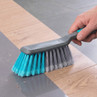 Blue and grey cleaning brush sweeping debris from tile and wood floor