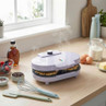 Purple waffle maker on kitchen worktop, steaming, with baking ingredients nearby