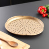 Gold non-stick pizza tray with holes, on kitchen surface