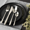 Four-piece silver cutlery set with patterned handles on black plate, styled with flowers