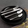 Four-piece stainless steel cutlery set with textured handles on black plate