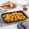 Black baking tray of cooked potato wedges on kitchen counter with utensils and fresh veg.