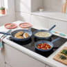 Set of three non-stick frying pans cooking chicken, creamy sauce, and tomatoes on a hob.
