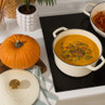 Cream cast iron casserole dish filled with pumpkin soup, shown on a hob beside a fresh pumpkin.