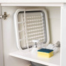White plastic dish rack with brush and sponge, stored on kitchen cupboard shelf.