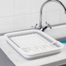 White collapsible dish drainer with raised spikes shown in a kitchen sink