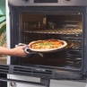 Hand placing margherita pizza on tray into oven