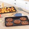 Non-stick black baking tray with chocolate cookies on kitchen counter