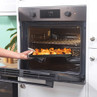 Hand placing tray of roast potatoes into a built-in electric oven