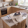 Compact ironing board with dog pattern and person ironing beige jumper in kitchen