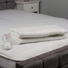 Folded white electric underblanket with attached control unit on a bed