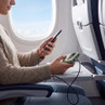 Person using green portable charger to power phone on airplane tray table