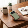 Green portable power bank held in hand on wooden desk, showing battery display.