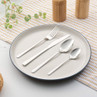 Four-piece stainless steel cutlery set on a cream plate, shown for product listing.