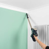 Cordless vacuum cleaning a ceiling corner in a modern room with pale green wall