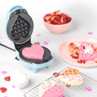 Blue heart-shaped waffle maker with pink waffle, served with strawberries and cream.