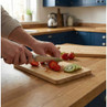 Person slicing strawberries and kiwi on a wooden chopping board in a kitchen