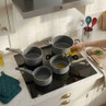 Set of four grey saucepans on induction hob, oil being poured into one pan