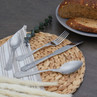 Set of four silver patterned cutlery pieces on placemat with bread in background