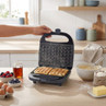 Waffle maker with two cooked waffles on kitchen counter, surrounded by baking ingredients.
