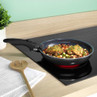 Black non-stick frying pan on induction hob cooking chicken with vegetables