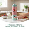 Mint green portable blender with smoothie, button being pressed in modern kitchen.