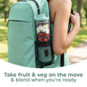 Portable blender cup with fruit and veg in a green backpack side pocket outdoors.