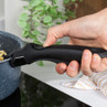 Close-up: black detachable handle held, attached to blue speckled saucepan in kitchen.