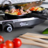 Giles & Posner raclette grill with filled mini pans, black control knob, and fresh ingredients.