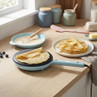 Light blue electric crepe maker on worktop with cooked crepes and batter in kitchen setting