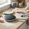 Blue electric crepe maker on kitchen counter, next to bowl of batter and baking ingredients