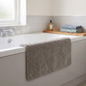 Neutral grey bath mat draped on white bathtub, fresh towels stacked beside soap.