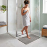 Grey bath mat in front of shower, shown in modern bathroom with woman stepping out