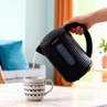 Black electric kettle pouring hot water into patterned mug on kitchen table