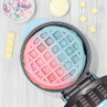 Ombre pink and blue waffle in waffle maker with white chocolate and mermaid sprinkles.