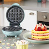 Open blue waffle maker with freshly cooked colourful waffles and berries on plate.