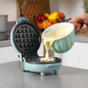 Teal waffle maker open with batter being poured in, shown on kitchen counter