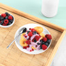 Plate of mini doughnuts topped with berry yoghurt, raspberries, blueberries and pomegranate seeds.