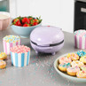 Purple mini donut maker on kitchen counter surrounded by colourful decorated mini donuts and sprinkles